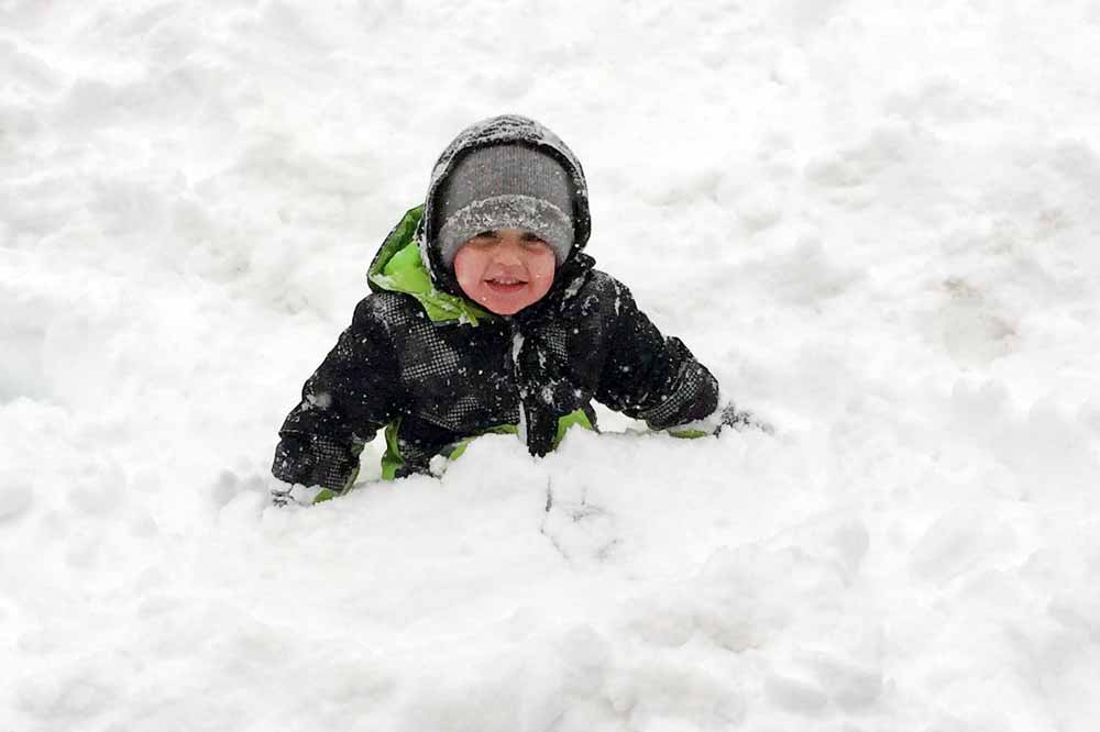 A young boy sits in the snow smiling.