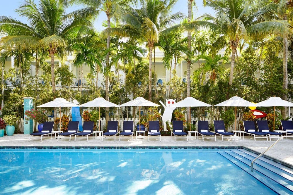 A blue pool surrounded by palm trees and lounge chairs at Parrot Key Hotel and Villas, one of the best family hotels in Key West and the Florida Keys.