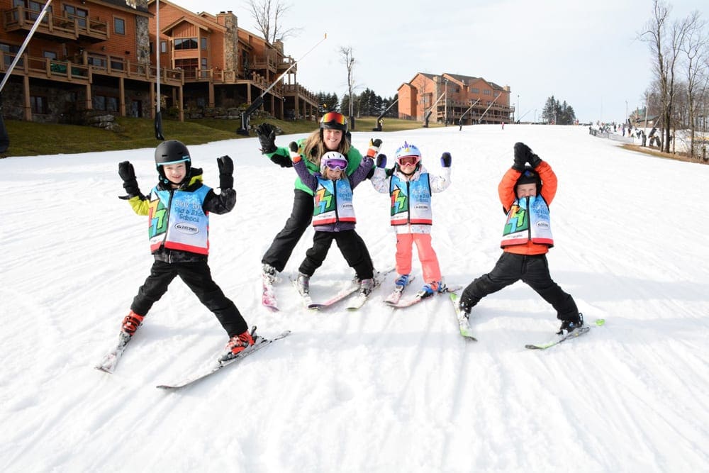 A ski instructor stands with four excited kids on skis along a slope at Seven Springs Mountain Resort, one of the best options for skiing near DC with kids.