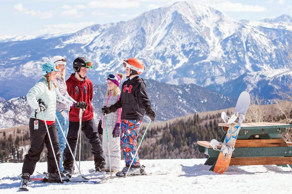 A family of four outfitted in snow gear and skis stands in the snow at Sunlight Mountain Resort, best small ski resorts in Colorado for families.