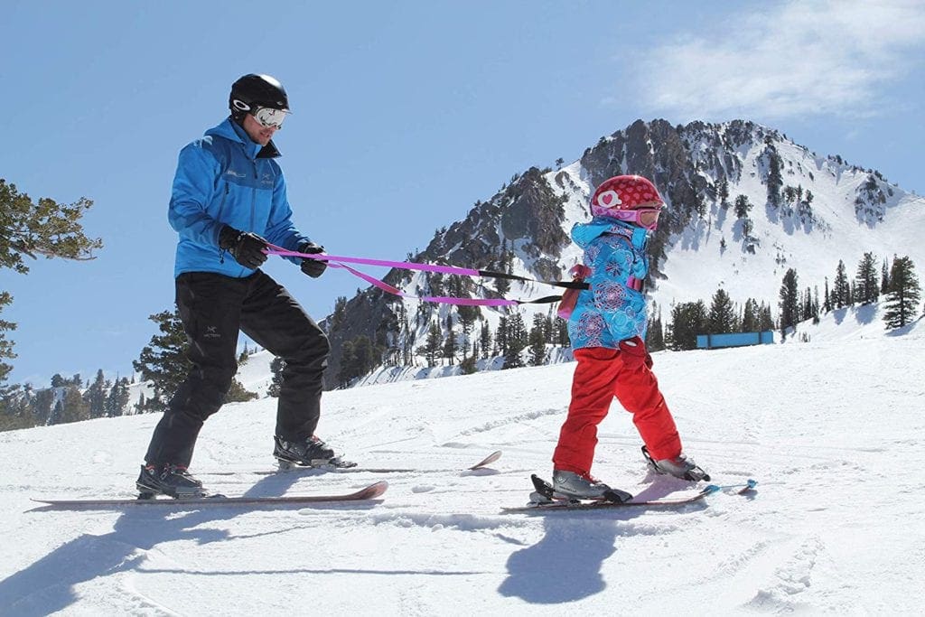 A dad holds his young child using a learn to ski harness.