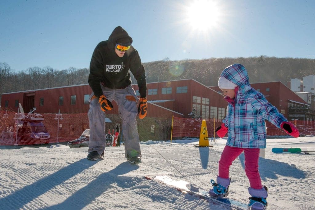 An adult looks at a young skier on a sunny day at Bear Creek Mountain Resort, one of the best resorts in Pennsylvania for families.