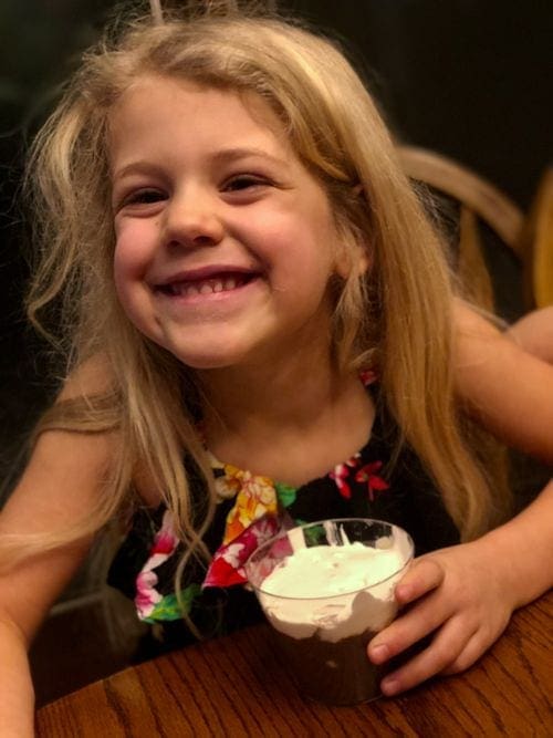 A young blond girl smiles while eating Chocolate Creme.