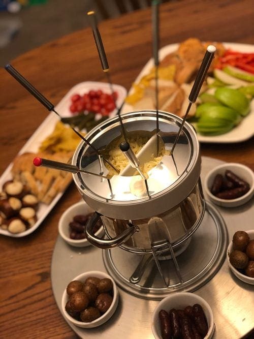 A fondue pot sits in the center of several dipping options, including apples, pretzels, tomatos, and more.