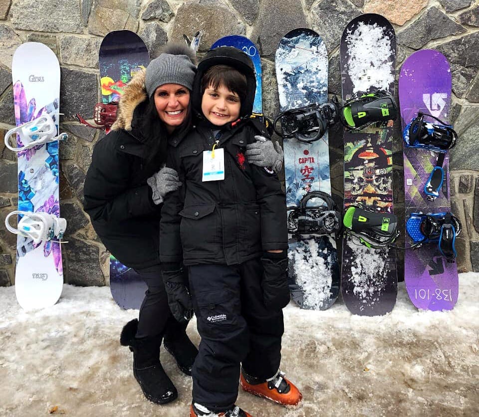 A mom hugs her young son in front of a series of colorful snowboards at Mount Snow in Vermont, one of the best family ski resorts in Vermont.