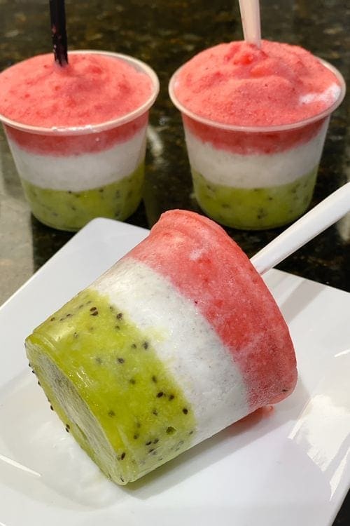 A plated Mexican paleta sits before two addtional ones on the counter, featuring layers of red, white, and green.