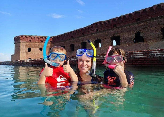 A mom holds both children, all wearing snorkel gear, with their heads out of the water in Dry Tortugas National Park.