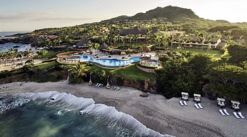 A view of Four Seasons Resort Punta from the oceanside, featuring waves and lush green grounds.