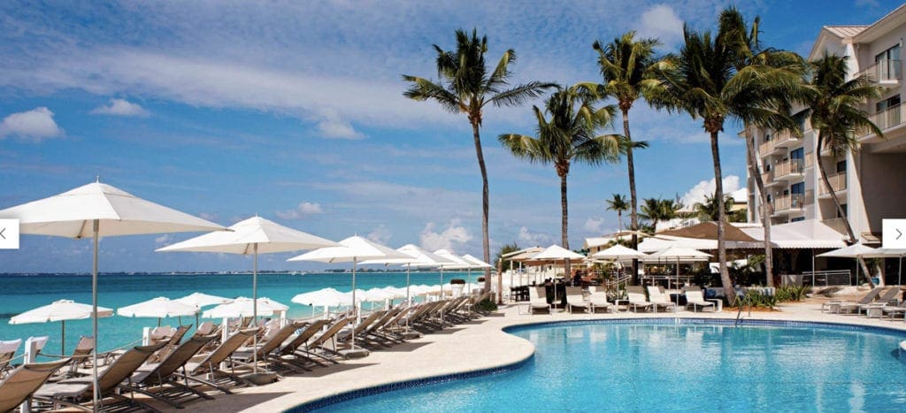 A pool at Grand Cayman Marriott Beach Resort, surrounded by beach chairs and palm trees at one of the best Marriott Resorts in the Caribbean for families.