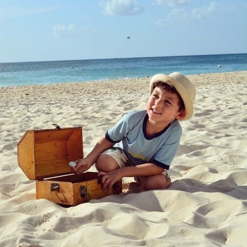 A young boy sits on the sand playing with a treasure chest at Grand Cayman Marriott Beach Resort.
