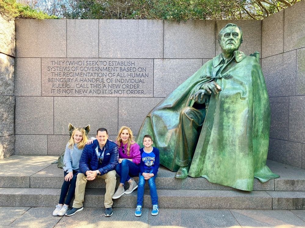 A family of four sits together near a statue in Washington DC.
