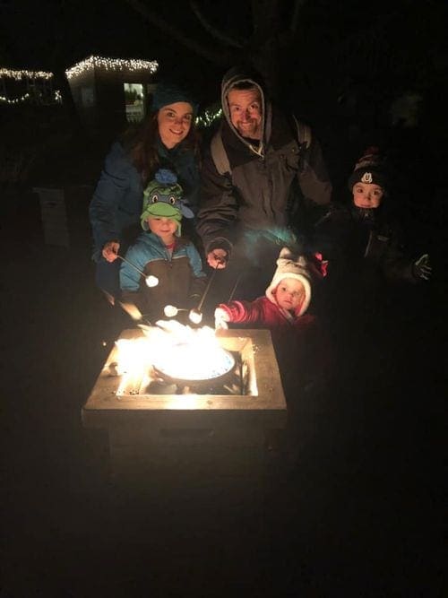 A family of five stands near a bonfire, roasting marshmallows at Crystal Springs.