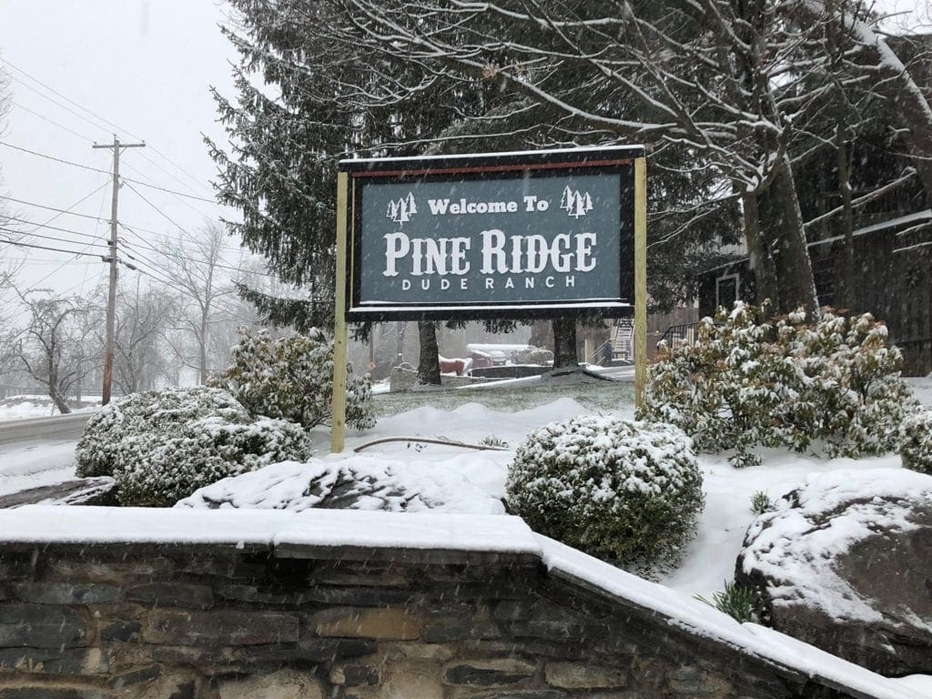 Entrance sign to Pine Ridge Dude Ranch, one of the best family resorts near NYC for a winter getaway, covered in snow.