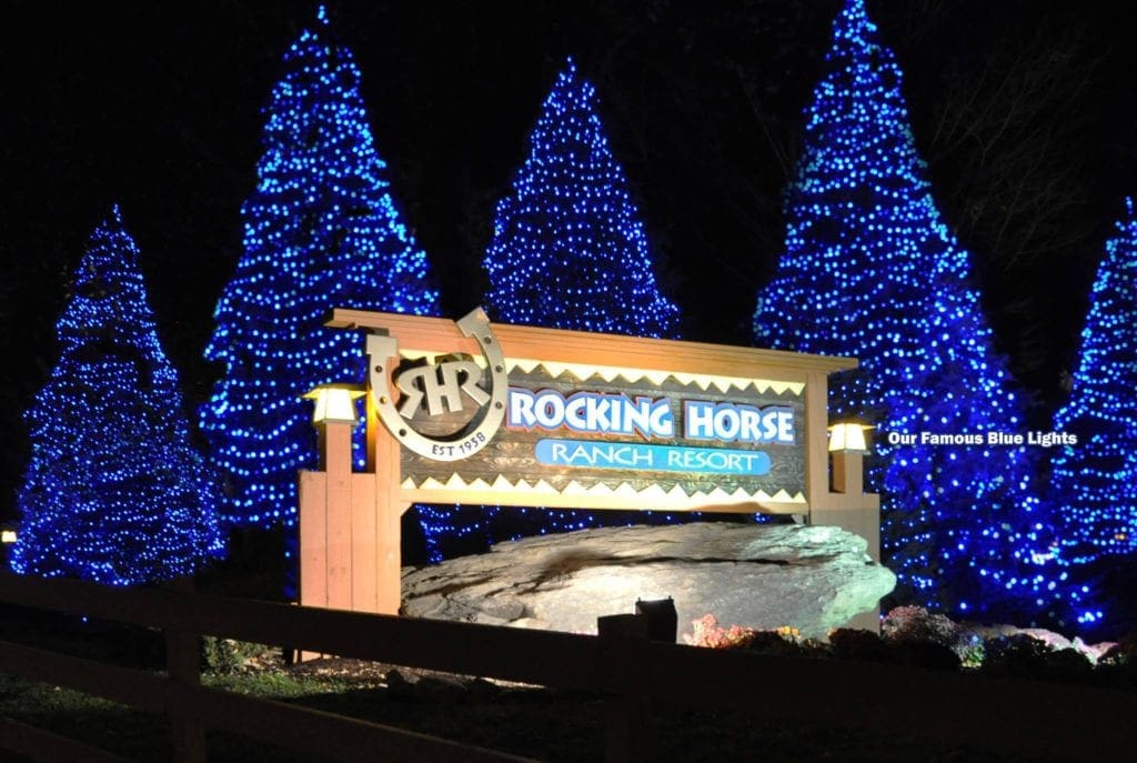 The sign for Rocking Ranch lit up at night and surrounded by blue-lit Christmas trees.