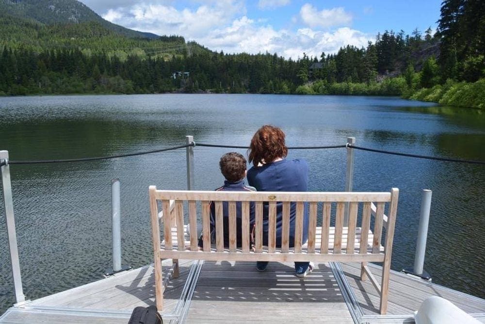 A mom and her young son sit on a bench admiring a lake near Whistler.