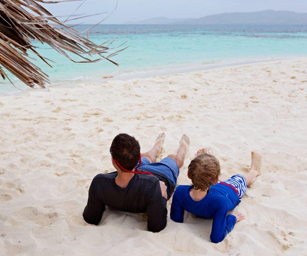 Father and son sit together on a beach in the Cayman Islands.