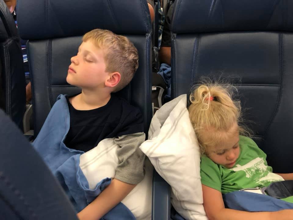 A boy and a girl siblings sleeping on airplane seats with pillows and blankets