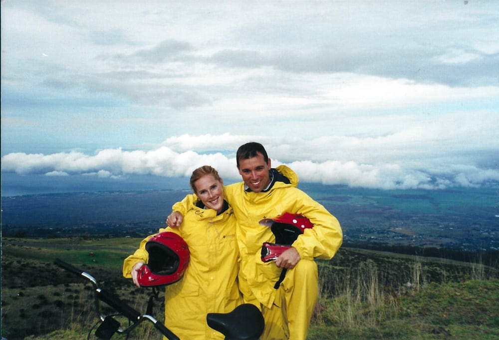 A couple, wearing yellow rain jackets, stands aside a road near their bikes on a bike tour of Haleakala.