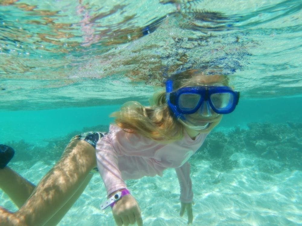 A young girl with a blue snorkel mask enjoys clear waters in the Maldives.