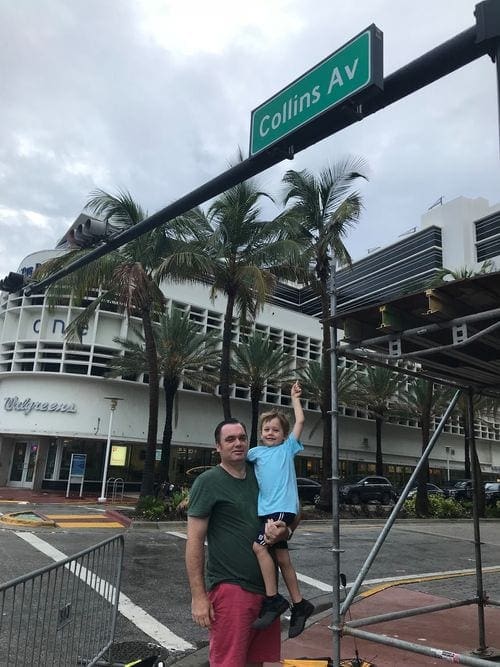 A dad and his young son stand under a sign for Collins Av off the strip at South Beach.