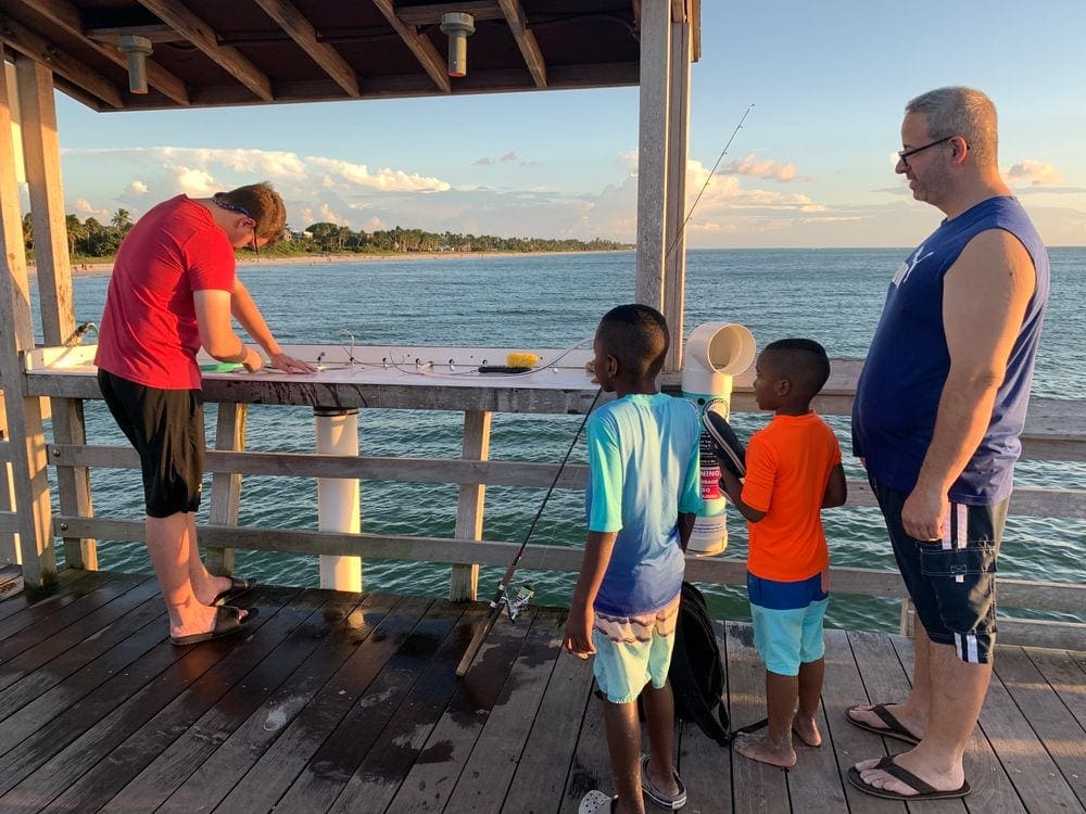 Two young black boys and their father enjoy watching a fisherman on the Naples Pier.