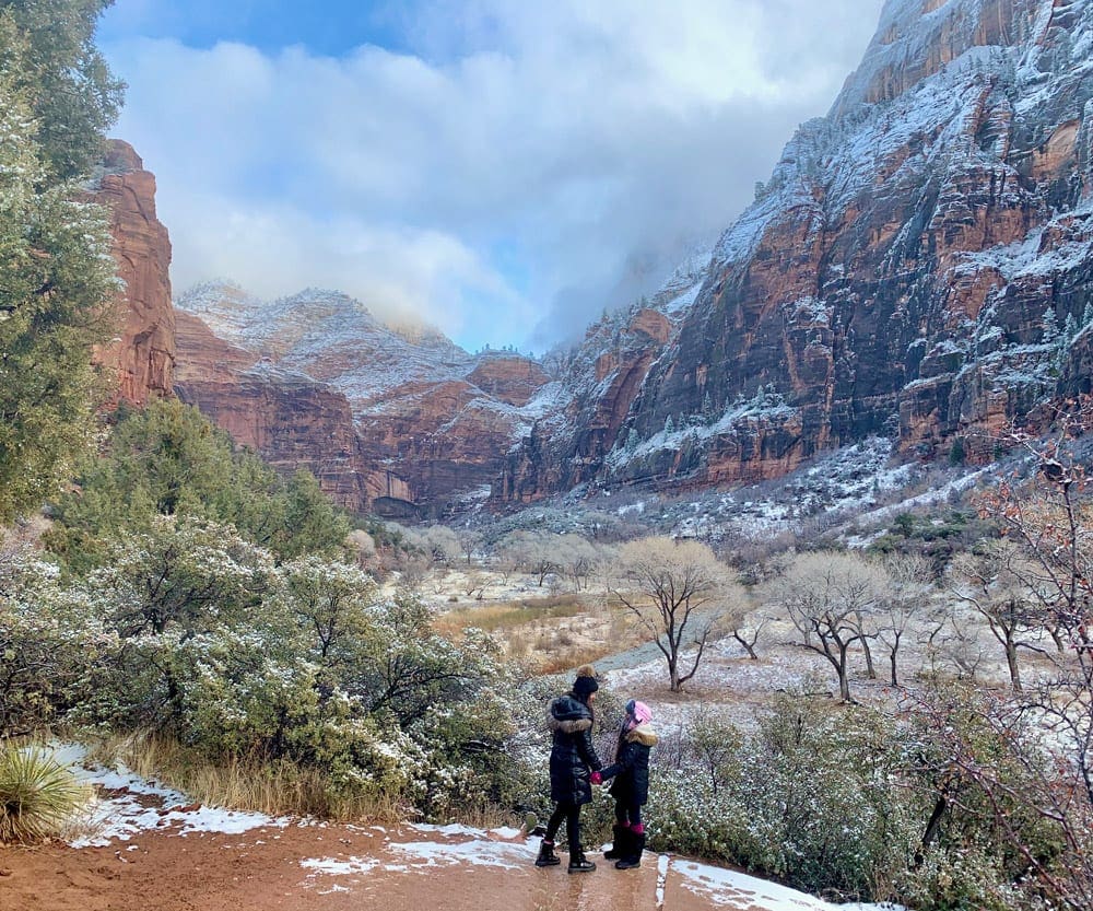 Mother and daughter stand together with an expansive view of Zion National Park behind them.