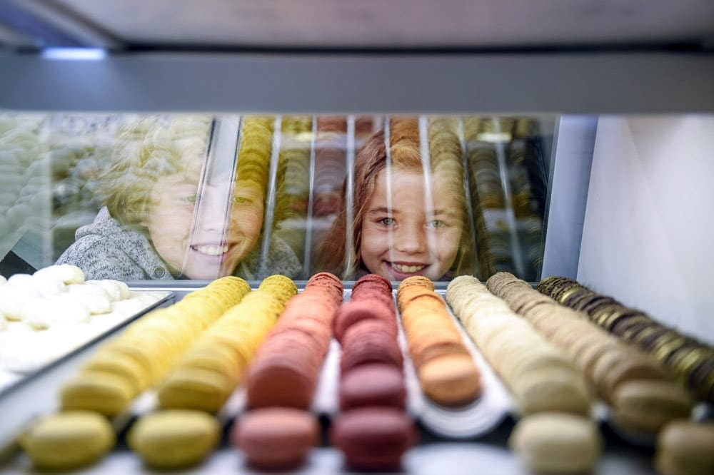 Two kids smile while gazing into a pastry case featuring macrons while on an Adventures by Disney tour.