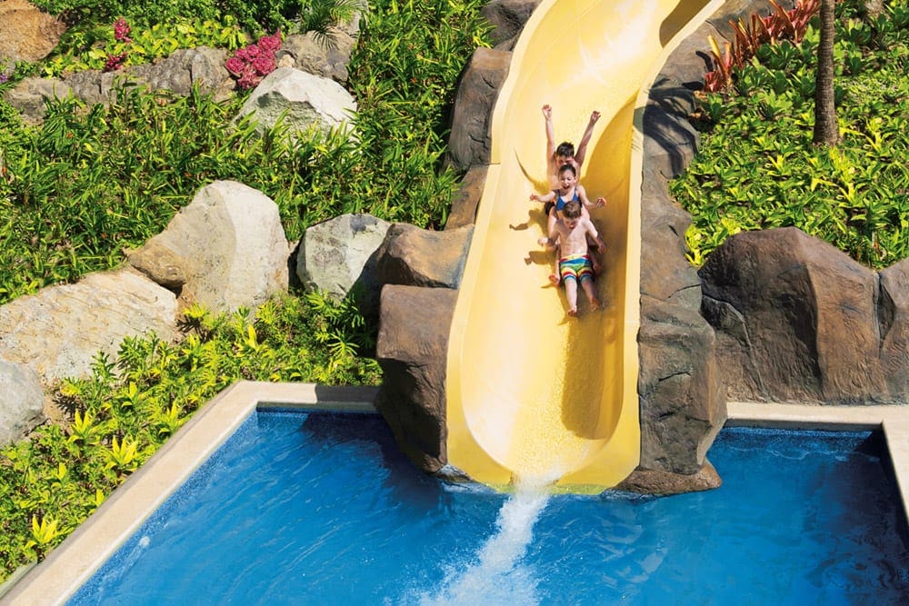 Three kids excitedly slide down a water slide at Dreams Las Mareas Costa Rica.