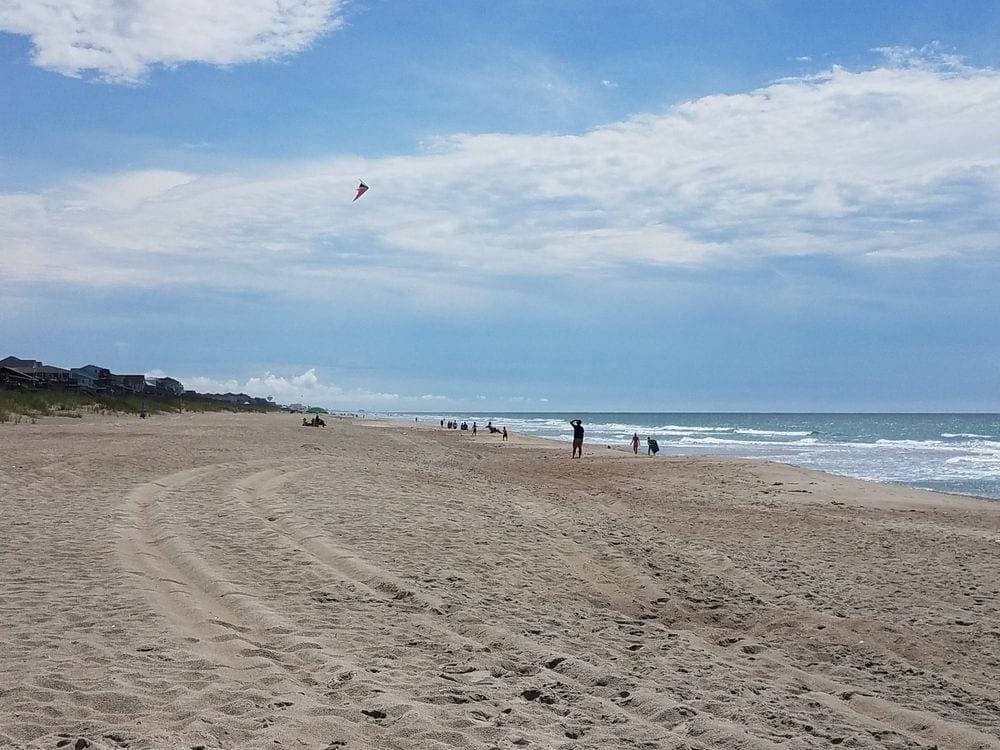On Emerald Isle, one of our recommended kid-friendly U.S. beaches for families, a man flies a kite in the distance on a clear day.