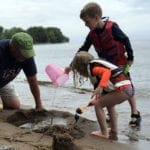 A grandpa and two kids play in the sand at Lake Mill Lacs.