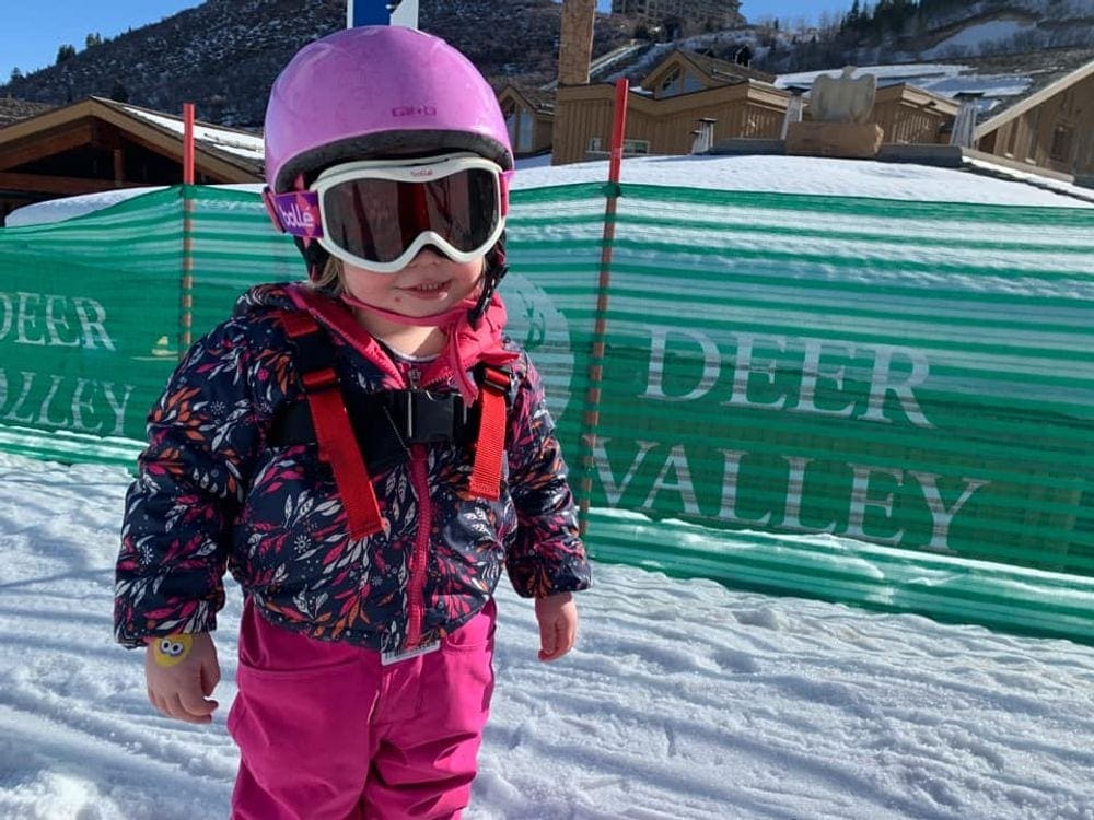 A young girl in snow gear, a helmet, and ski goggles enjoys a sunny day at Deer Valley.