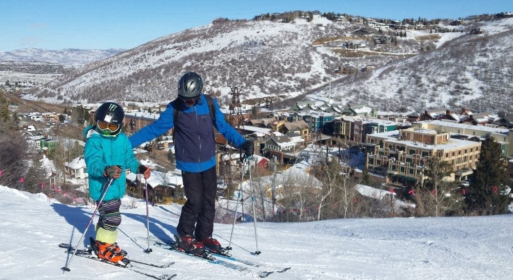 A father and son ski with the mountains behind them in Park City, Utah.
