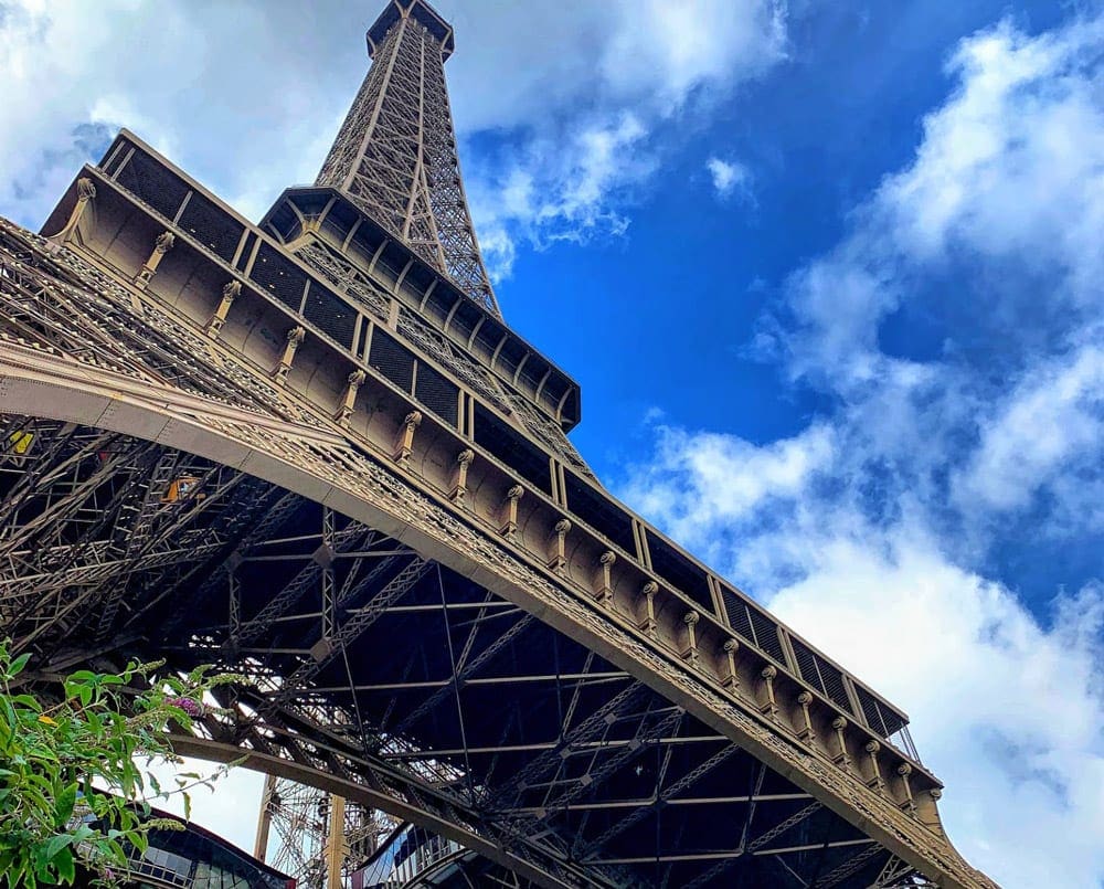A view of the Eiffel Tower in Paris looking up from under the Parisian landmark with blue skies above.