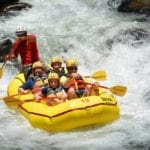A yellow raft going down a Costa Rican river, carrying four passengers and a guide while on an Adventures by Disney tour.