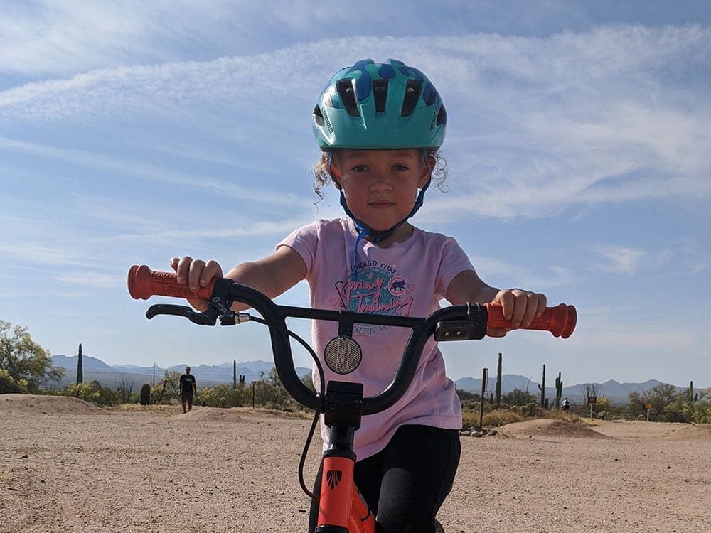 A young girl wearing a blue helmet holds onto her handle bars while stradeling her bike on a trail at McDowell, near Phoenix.