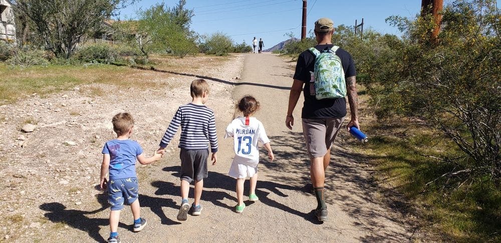 A dad and his three kids hike along a desert trail.
