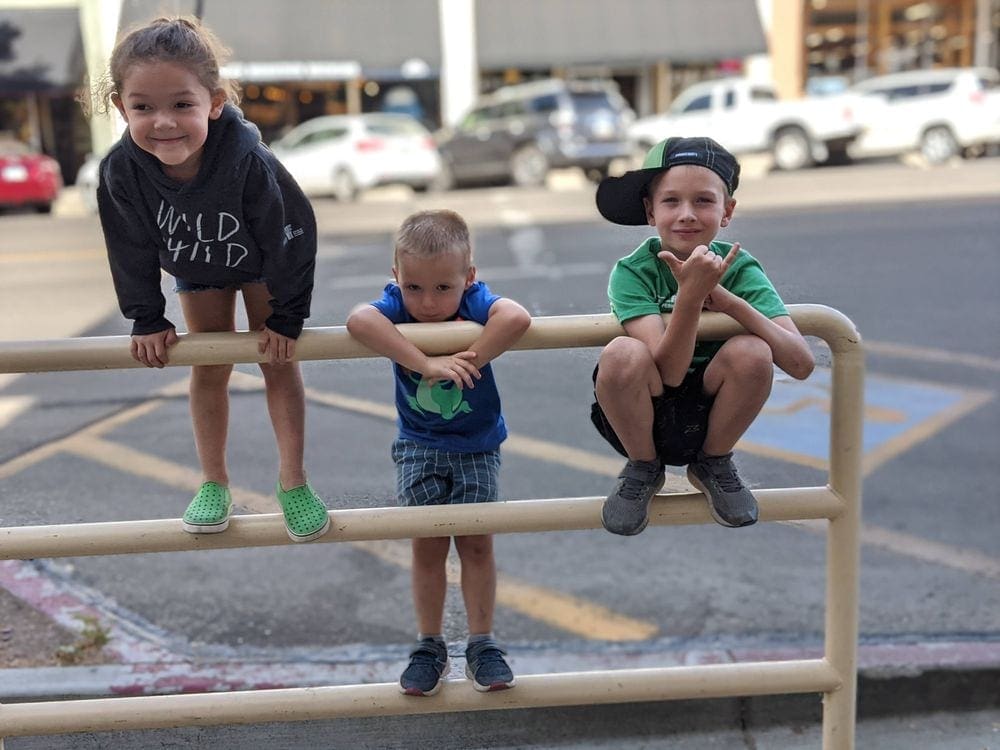 Three kids climb and pose on a metal railing in Prescott.