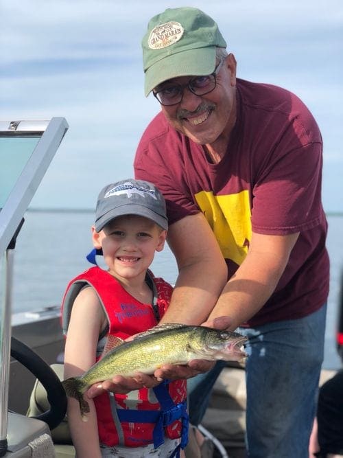 A grandpa holds a fish caught on Lake Mille Lacs while his grandson smiles proudly.