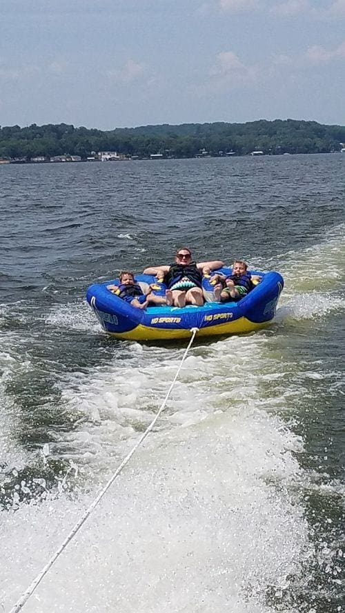 A tube pulling an adult and two kids behind a boat wake on Lake of the Ozarks.
