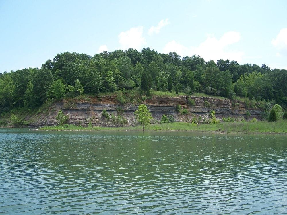 Lake Patoka on a sunny day, with a forested rock formation in the background.