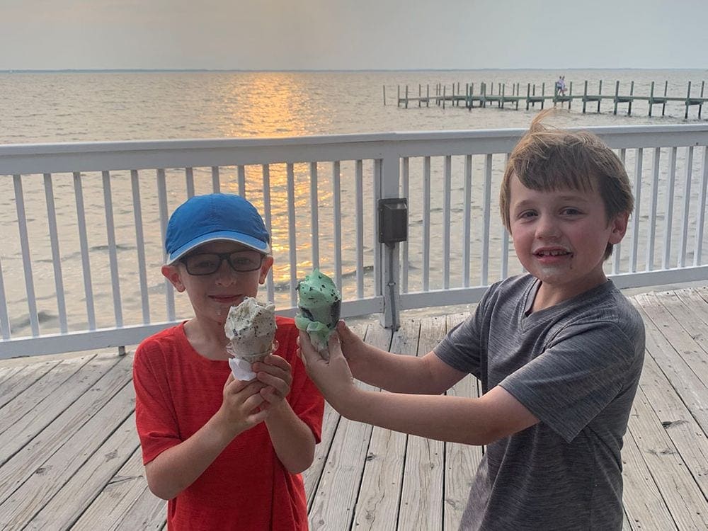 Two young boys hold ice cream cones on a boardwalk in the Outer Banks at sunset.