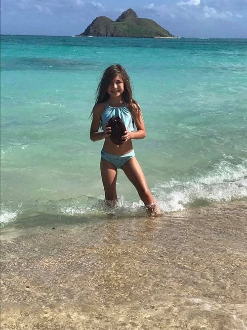 A young girl in a bikini stands on Lanikai Beach in Hawaii.