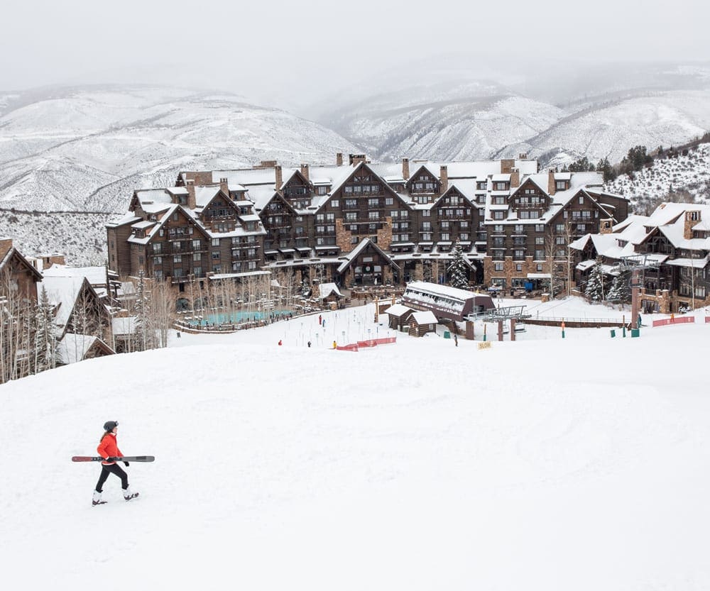 A teen with an orange coat carries skis across the grounds at The Ritz-Carlton, Bachelor Gulch.