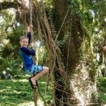 A young boy hangs on a vine while exploring the Road to Hana.
