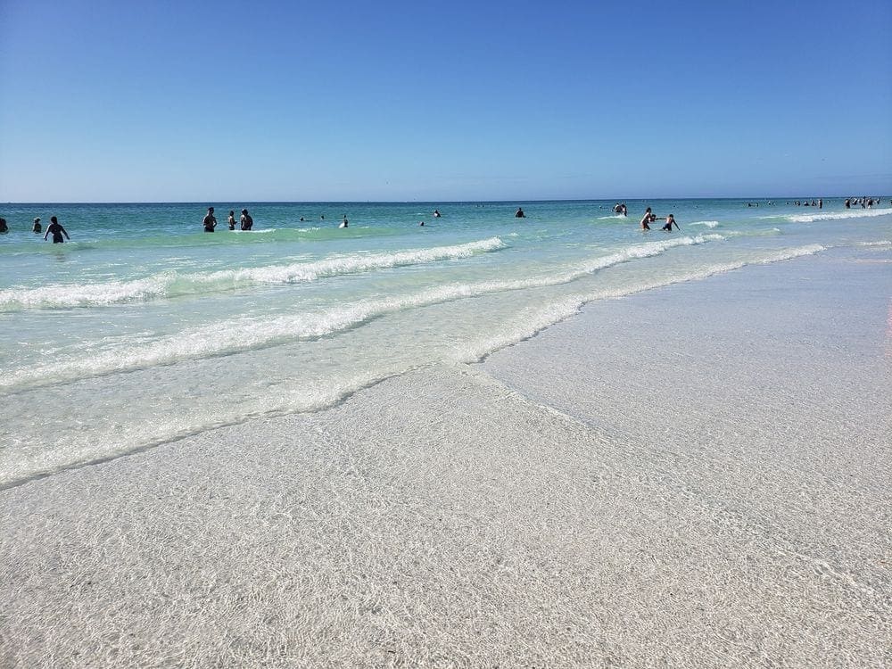 Several people anonymously dot the shoreline of Siesta Key on a sunny day, one of our recommended kid-friendly U.S. beaches for families.