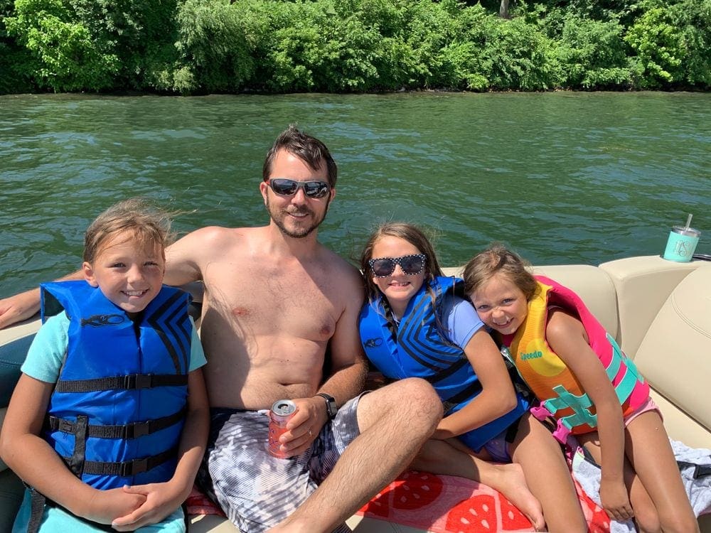 A dad sits with his three kids on a boat on Lake Geneva on a sunny day.