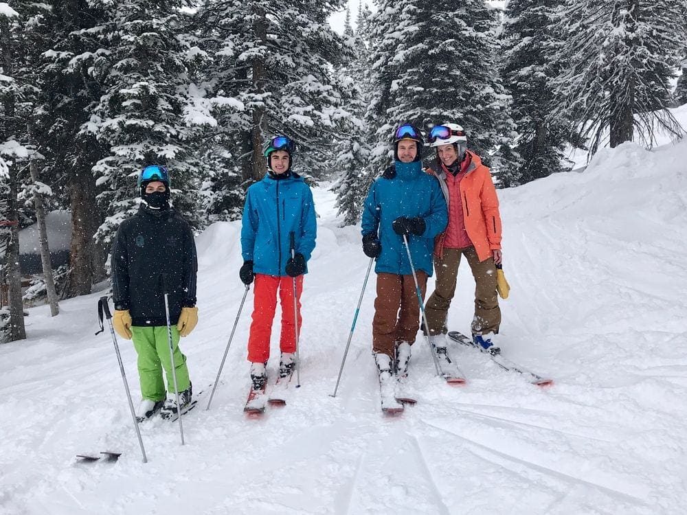 A family of four wearing skis and ski gear smiles at the camera while skiing at Jackson Hole.