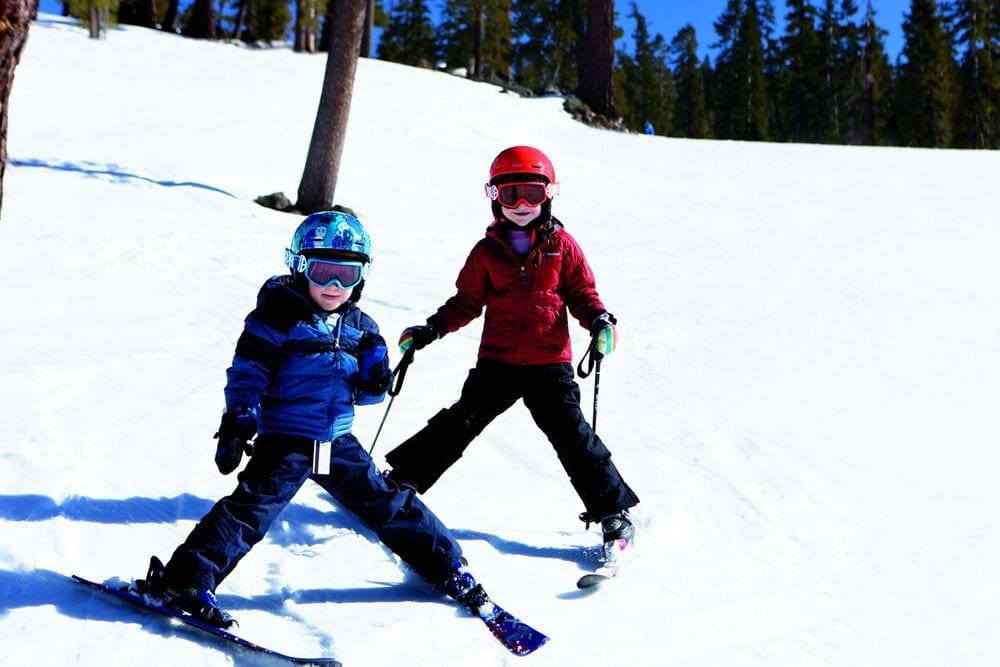 Two kids, one in blue and one in red, ski down a hill at The Ritz Carlton, Lake Tahoe.