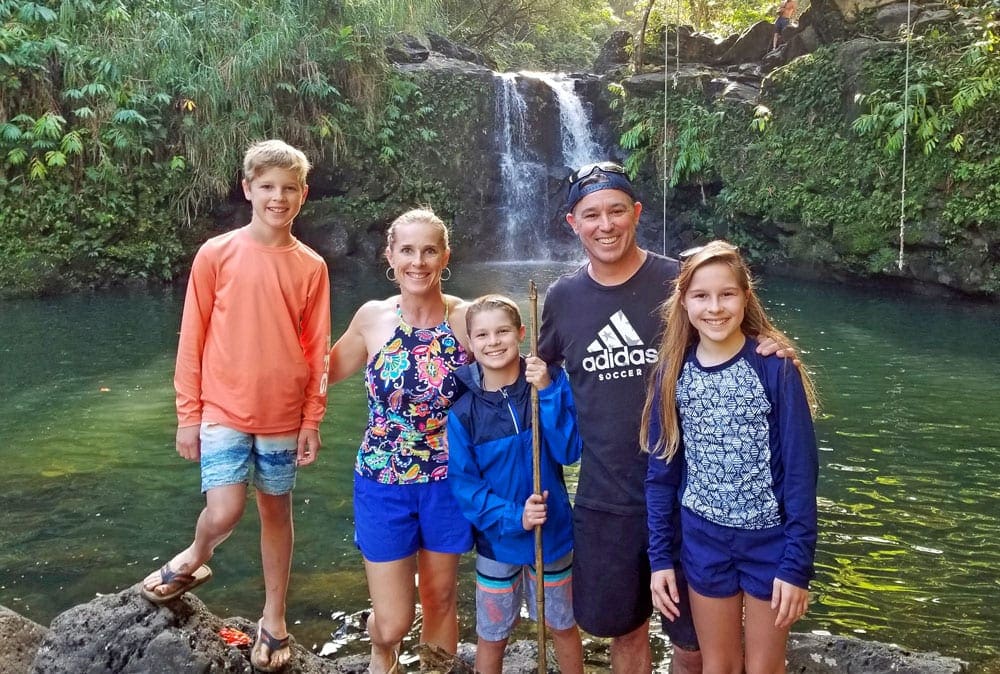 A family of five poses together, smiling, in front of Waikamoi Falls in Maui.