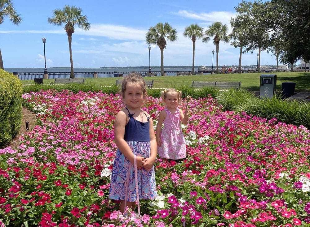 Two young girls stand in a field of flowers.